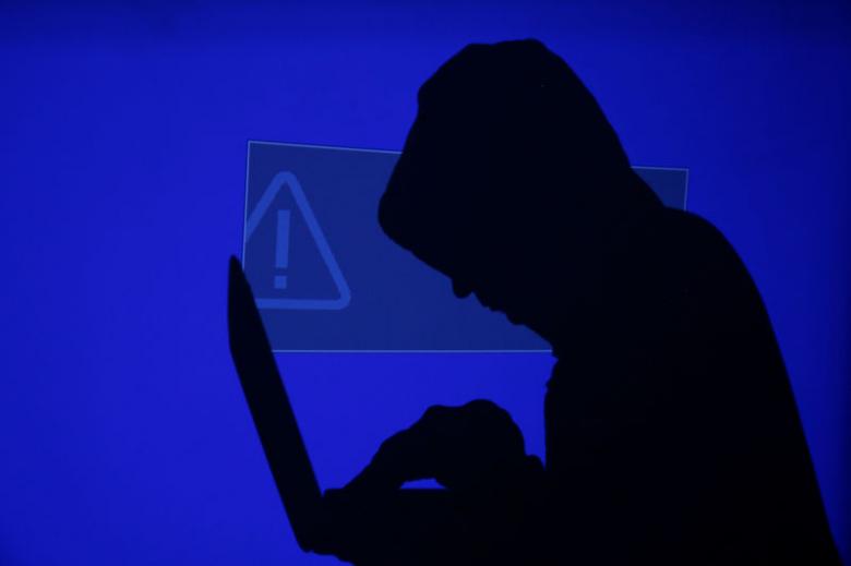A hooded man holds a laptop computer as blue screen with an exclamation mark is projected on him in this illustration picture taken on May 13, 2017. REUTERS/Kacper Pempel/Illustration