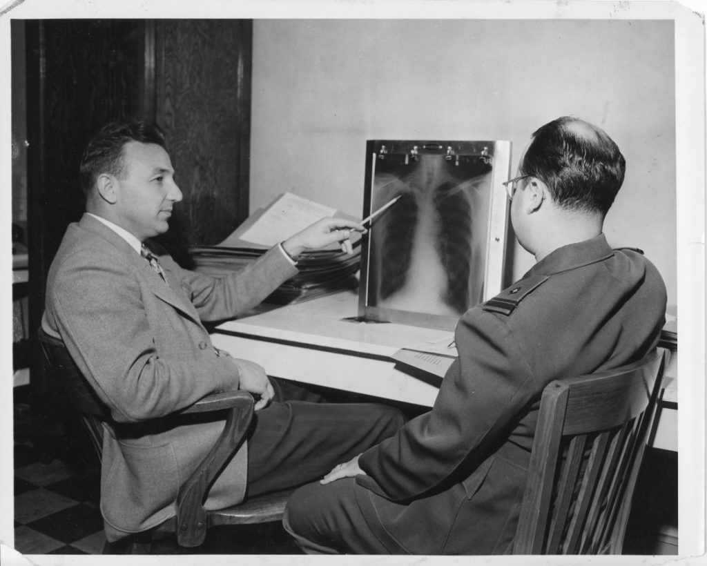 Black and white photo of two men looking at chest x-rays